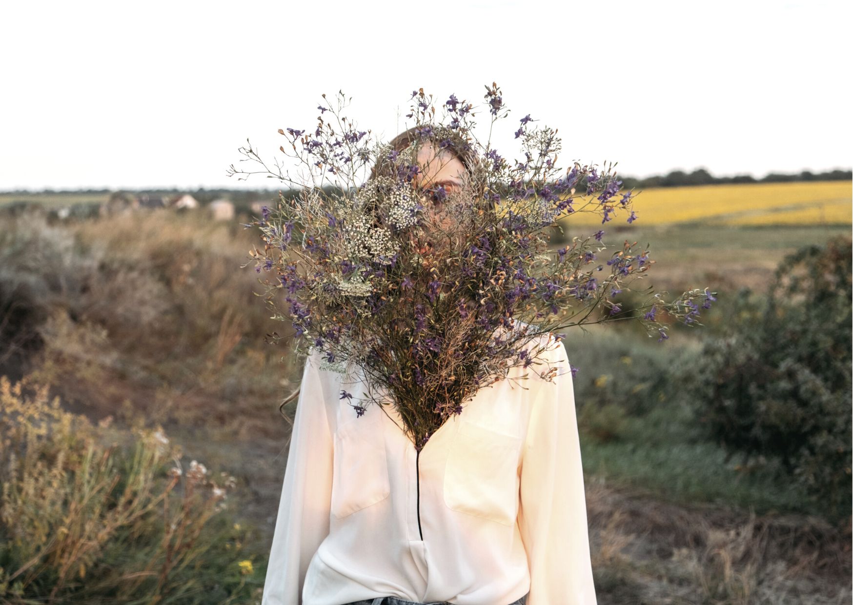 Femme dans un champ, le visage caché par un bouquet de fleurs séchées